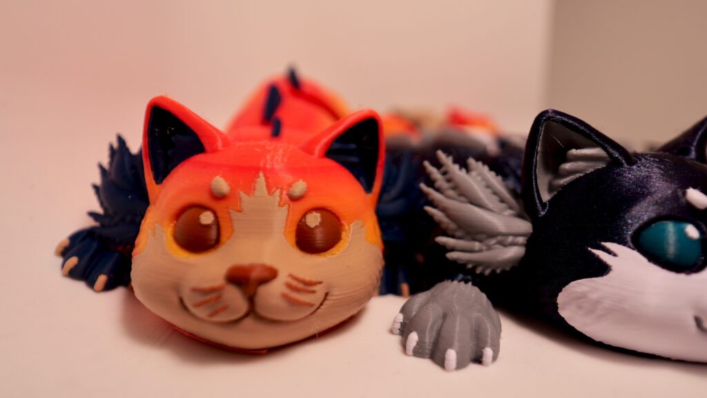 Several cat-like figures in orange, cream, black, and gray, with frilled details; a black-and-white figure is partly cropped.